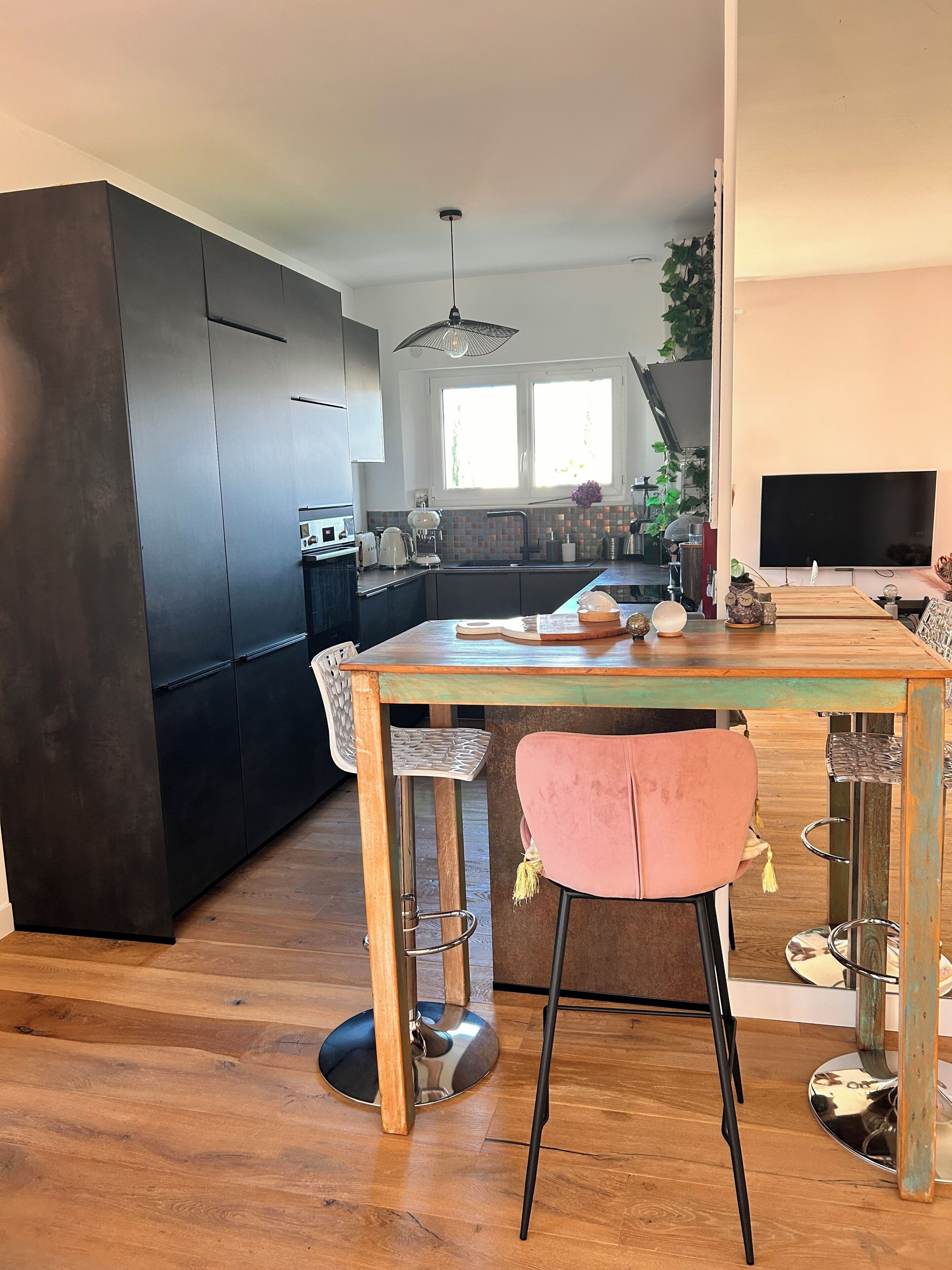 A modern kitchen with dark cabinets, a wooden dining table, and a pink chair.