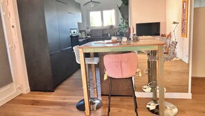 A modern kitchen with dark cabinets, a wooden dining table, and a pink chair. - The Good Life… (Fréjus)