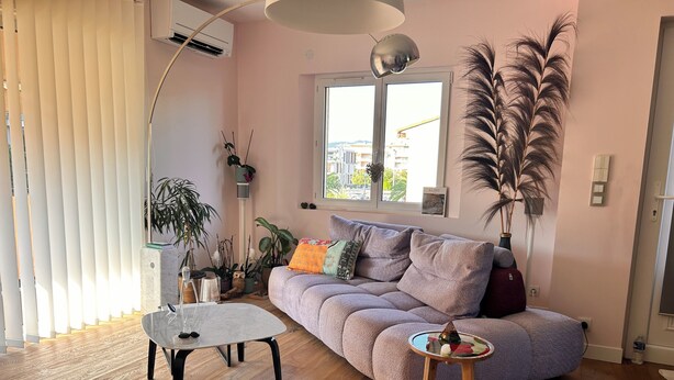 A cozy living room with a sofa, a coffee table, and a side table. There are potted plants and a lamp. - The Good Life… (Fréjus)
