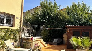 A patio area with a table and chairs, a small garden, and a wooden deck. - The Good Life… (Fréjus)
