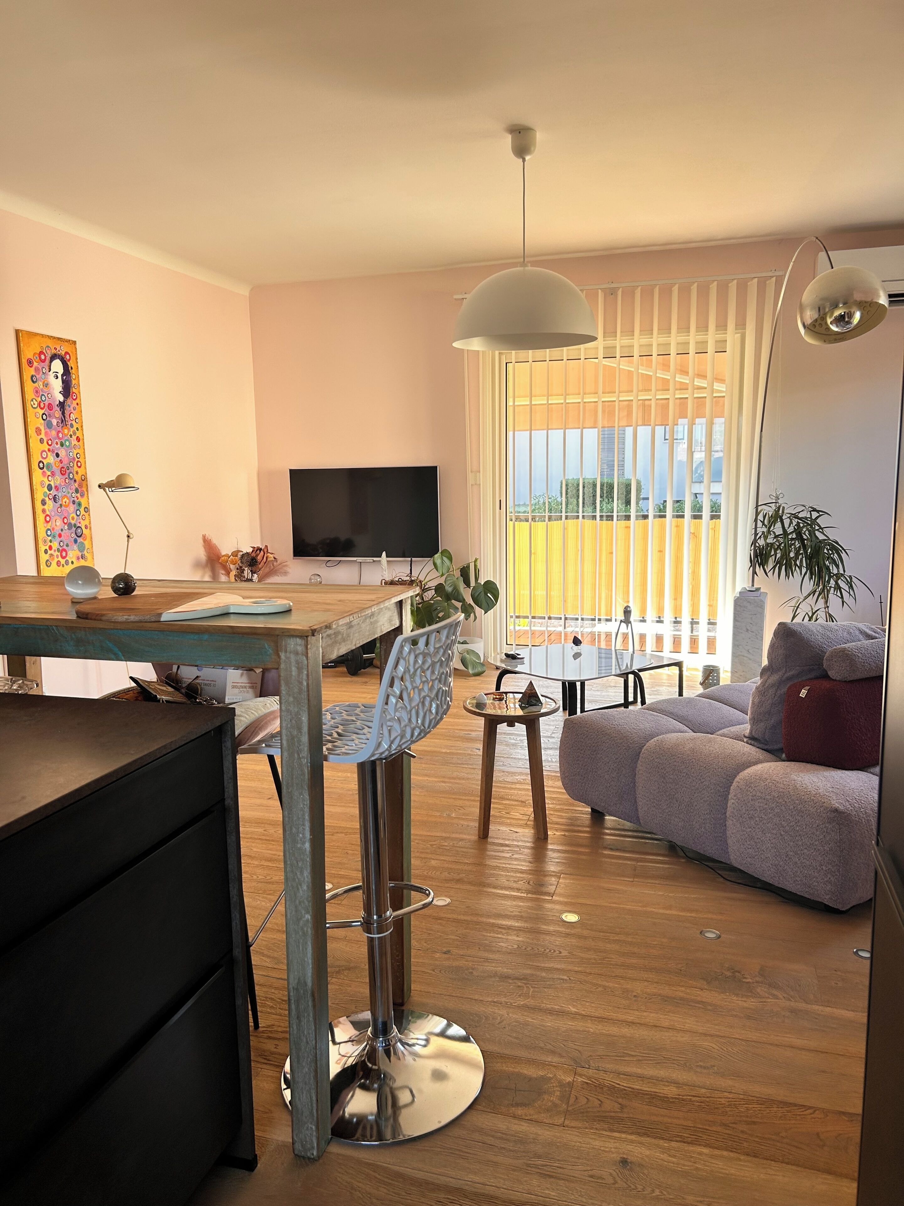 Uma sala de estar moderna com área de jantar, sofá, televisão e uma janela grande com persianas.