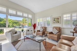 A spacious living room with a large window, a coffee table, and leather sofas. - Bradman View | Bowral Garden and Fireplace Retreat (Bowral)