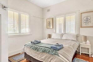 A bedroom with a bed, two bedside tables, a window with blinds, and a framed picture on the wall.