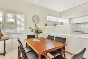 A dining room with a wooden table and chairs, a vase with flowers, and a clock on the wall. - Bradman View | Bowral Garden and Fireplace Retreat (Bowral)