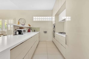 A modern kitchen with white cabinetry, a microwave, a kettle, and a clock on the wall.