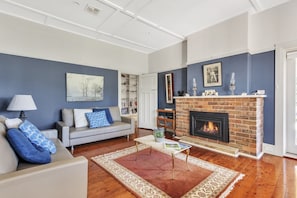 A living room with a fireplace, a sofa, a coffee table, and a bookshelf. - Bradman View | Bowral Garden and Fireplace Retreat (Bowral)