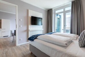 Une chambre d’hôtel moderne, équipée d’un lit, d’un téléviseur fixé au mur et d’une fenêtre avec des rideaux.