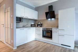 Une cuisine moderne avec des meubles blancs, un four à micro-ondes, une machine à café et une cuisinière.