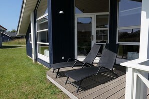 A deck with two lounge chairs and a table, overlooking a grassy area.