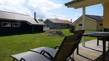 Eine Terrasse mit Tisch und Stühlen, eine Rasenfläche und im Hintergrund ein Gebäude mit rotem Ziegeldach.