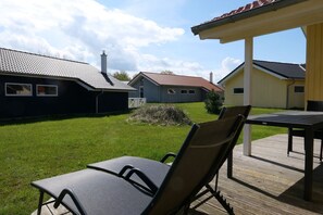 Eine Terrasse mit Tisch und Stühlen, eine Rasenfläche und im Hintergrund ein Gebäude mit rotem Ziegeldach.