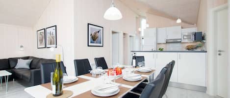 Un espace repas moderne avec une longue table dressée pour quatre personnes, entourée de chaises. Une bouteille de vin et des verres sont posés sur la table.