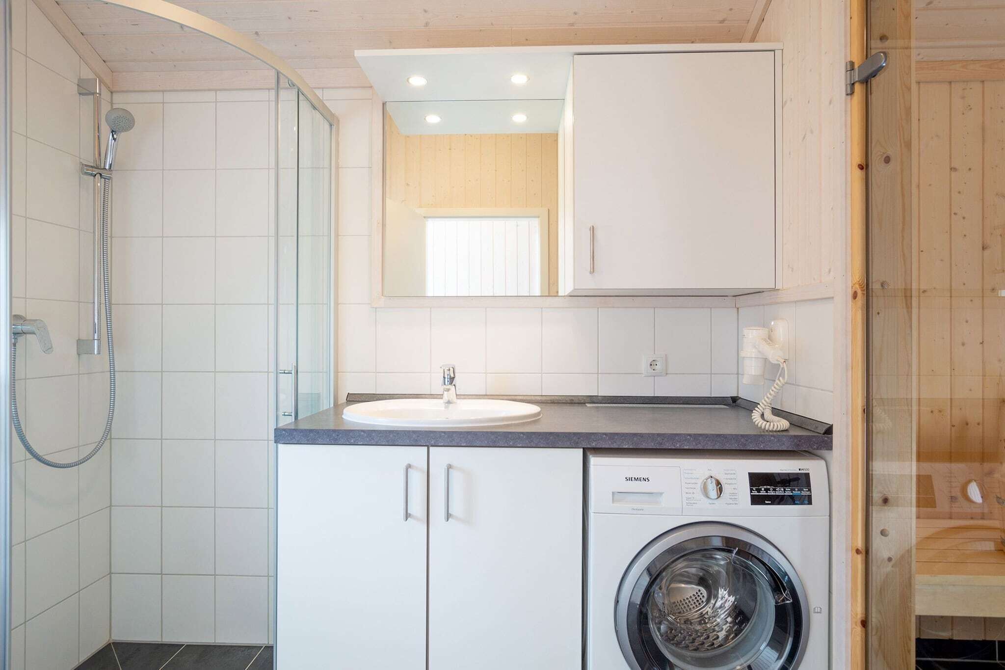 A compact bathroom with a shower, a sink, and a washing machine.