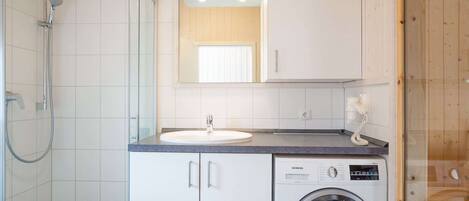 A compact bathroom with a shower, a sink, and a washing machine.