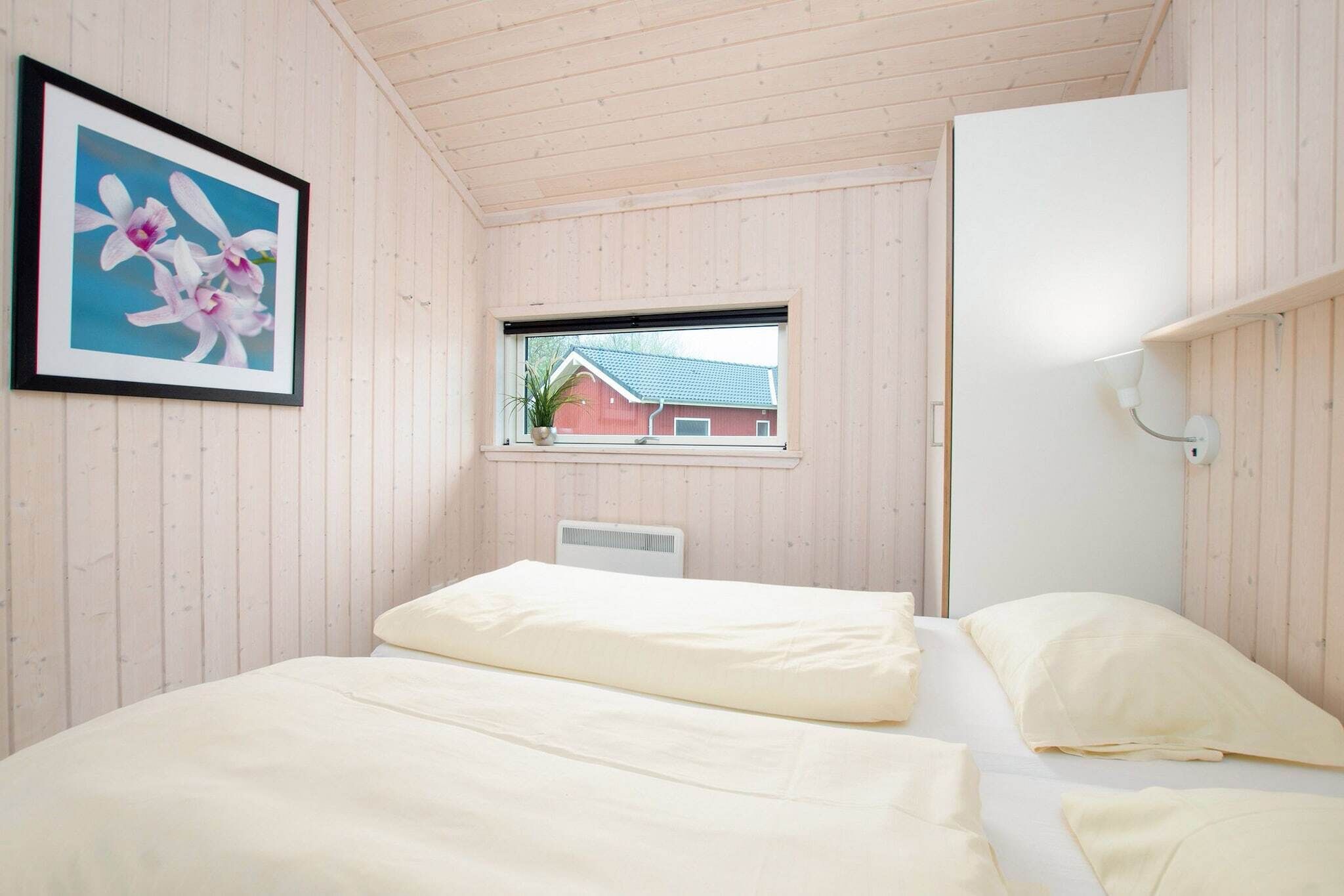 A bedroom with two beds, a window with a view of a red building, and a framed picture on the wall.