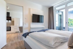 A hotel room with a bed, a TV mounted on the wall, a kitchenette, and a balcony with curtains. - Parkview Baltischer Kurzurlaub für 4 Personen (Travemünde)