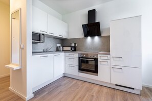 A compact kitchen with white cabinets, a microwave, a coffee maker, an oven, and a black range hood. - Parkview Baltischer Kurzurlaub für 4 Personen (Travemünde)