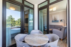 Ein modernes Zimmer mit Glastür zu einem Balkon, einem runden Tisch mit Stühlen und einem grauen Sofa.