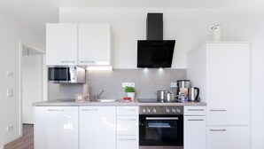 Uma cozinha moderna com armários brancos, micro-ondas, fogão e exaustor preto.