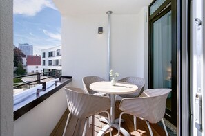 A balcony with a round table and four chairs, a potted plant, and a view of buildings. - Rückzugsort mit Parkblick (Travemünde)