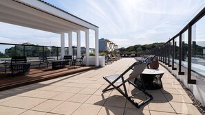 Terraço no telhado com área de estar ao ar livre, pérgola e vista para o horizonte da cidade.