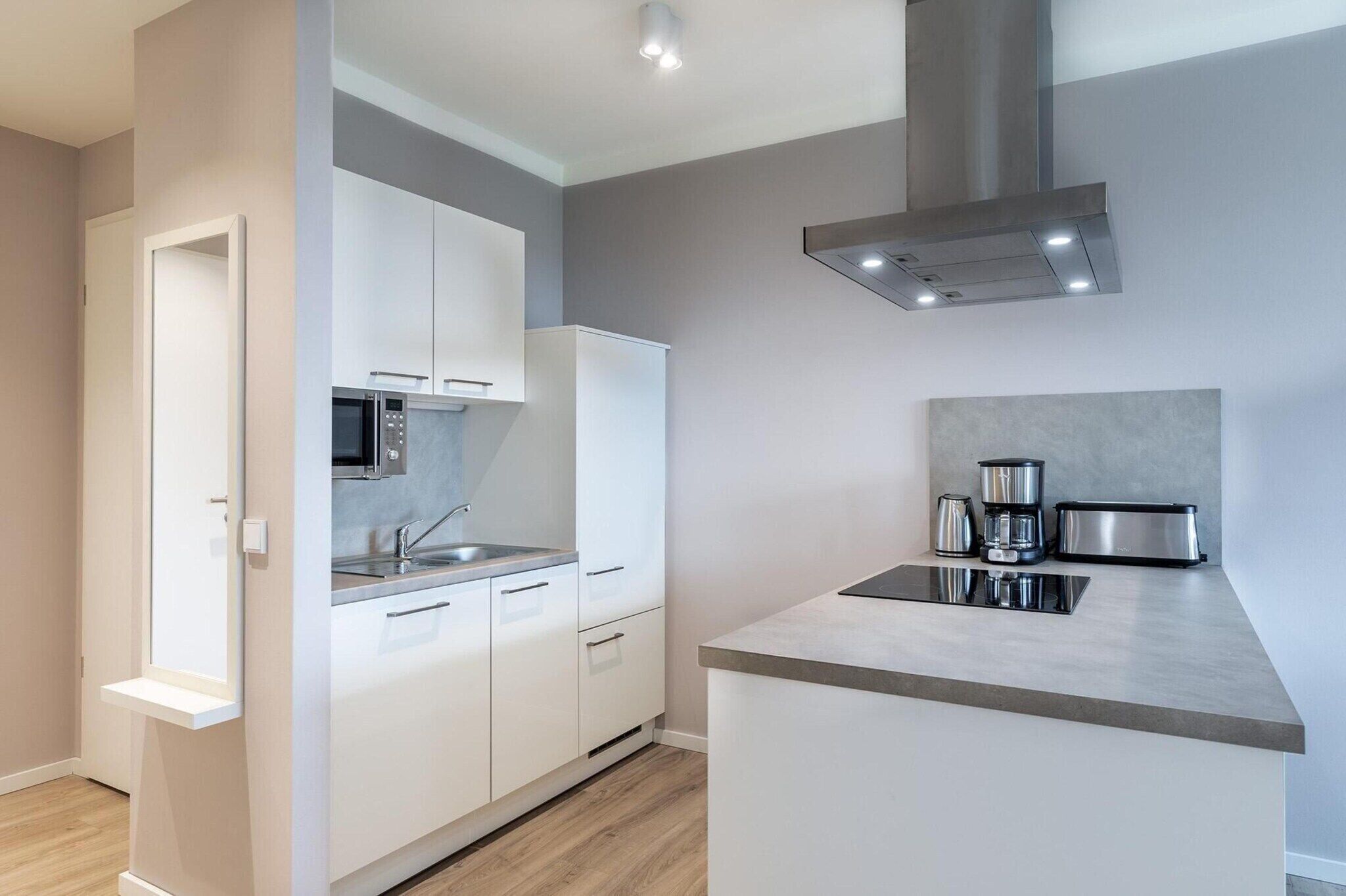 A modern kitchen with white cabinets, a microwave, a sink, and a coffee maker.