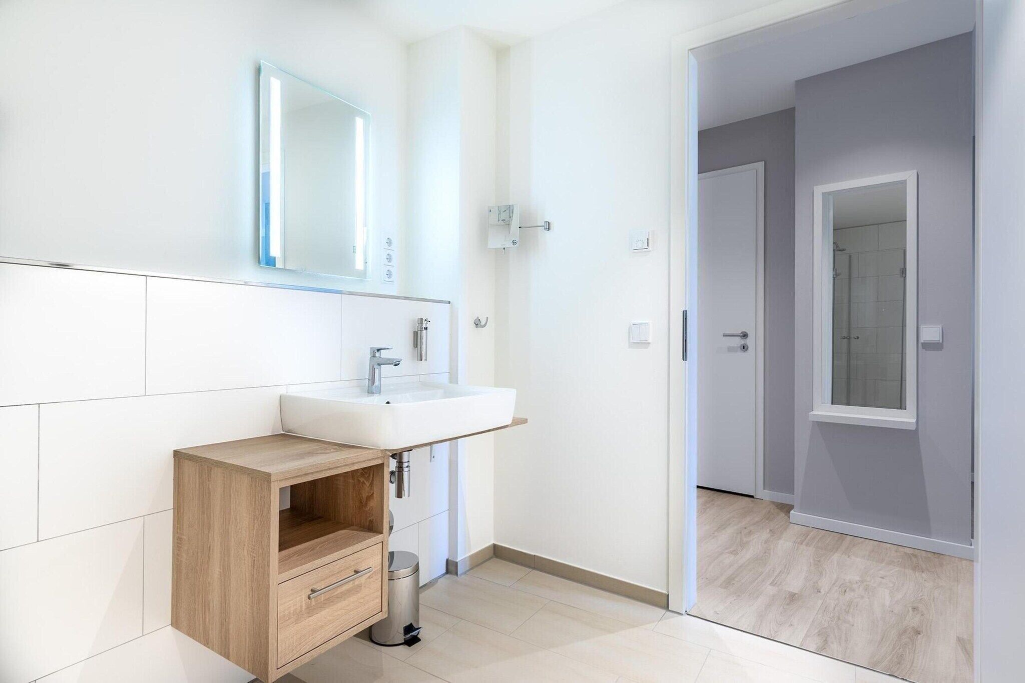 A modern bathroom with a white sink, mirror, and wooden cabinet.