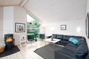 Una sala de estar moderna con chimenea, un sofá de cuero negro, una mesa de centro blanca y vistas a zonas verdes.