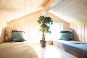 Acogedor dormitorio en ático con paredes de madera y techos inclinados, con dos camas y almohadas a juego, y una planta en maceta.