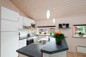 A modern kitchen with white cabinets, a black countertop, a stainless steel sink, and a window with a view of a red building. - Hübsches Cottage mit Kamin (Großenbrode)
