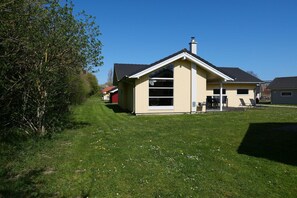A single-story house with a gabled roof, a chimney, and a covered porch with chairs. - Hübsches Cottage mit Kamin (Großenbrode)