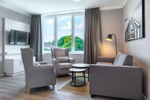 A modern living room with a flat-screen TV, grey sofas, a round coffee table, and a large window with curtains. - Apartment near the Baltic Sea (Travemünde)