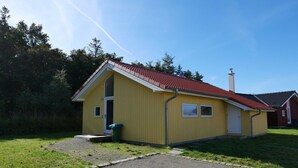 A yellow single-story building with a red-tiled roof, a chimney, and a small front porch. - Charming Seaside Haven Oasis für 6 (Großenbrode)