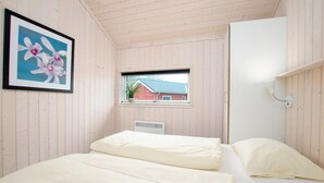A room with two beds, a window with a view of a red building, and a framed picture of flowers. - Charming Seaside Haven Oasis für 6 (Großenbrode)