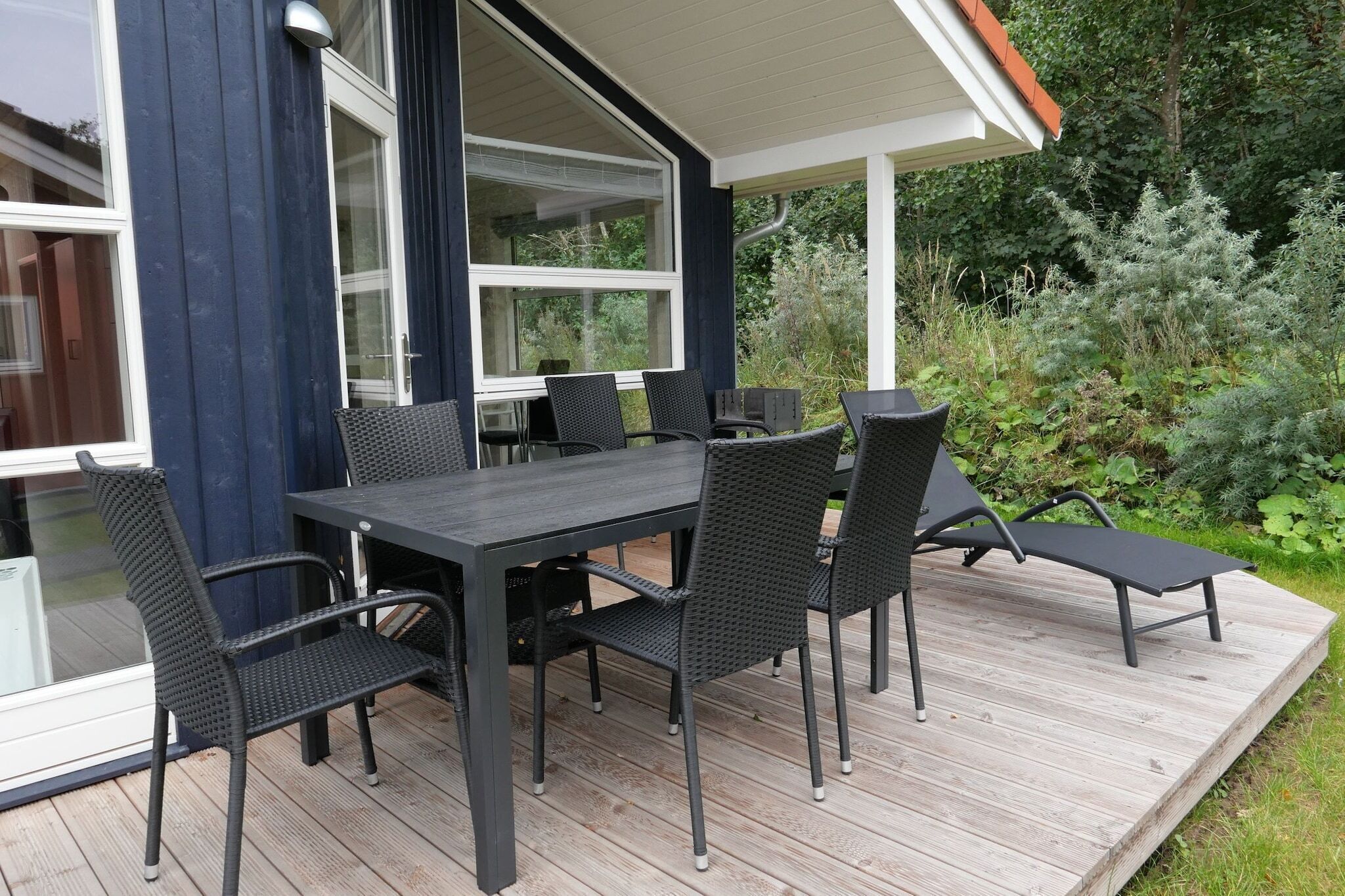 An outdoor patio with a dark-colored table and chairs, surrounded by greenery.