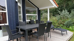 Um pátio externo com mesa e cadeiras escuras, cercado por vegetação.