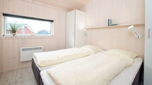 Quarto com duas camas, janela com vista para casas, radiador e prateleira com livros.