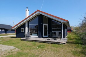 Una casa moderna amb una gran porta de vidre, un porxo cobert amb dues cadires i una xemeneia.