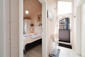 Une chambre à coucher comprenant un lit, une table de chevet, une étagère murale avec des livres et une fenêtre avec des stores.