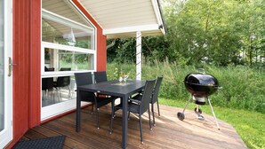 Eine Terrasse mit Tisch, Stühlen, einem Grill und einer Glastür zum Innenbereich.
