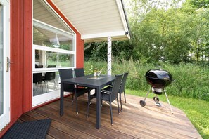 Eine Terrasse mit Tisch, Stühlen, einem Grill und einer Glastür zum Innenbereich.