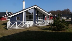 Ein einstöckiges Haus mit Satteldach, einer Veranda mit weißen Geländern und einem Schornstein.