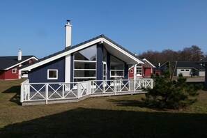 Ein einstöckiges Haus mit Satteldach, einer Veranda mit weißen Geländern und einem Schornstein.