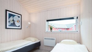 Ein Zimmer mit zwei Betten, einem gerahmten Blumenbild, einem Fenster mit Blick auf ein rotes Gebäude und einem Wandheizkörper.