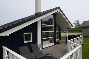Eine überdachte Terrasse mit Stühlen und einem Tisch, ein dunkelblaues Gebäude mit weißer Reling und ein klarer Himmel.