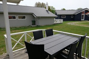 A covered outdoor patio with a table and chairs, a grassy lawn, and a building with a tiled roof in the background. - Gemütliches baltisches Versteck für 6 (Großenbrode)