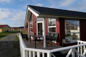 A building with a covered outdoor area featuring a table and chairs, a deck, and a view of the surrounding landscape. - Nordische Flucht nahe der Ostsee (Großenbrode)