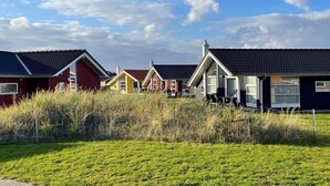 A row of single-story houses with pitched roofs, surrounded by a grassy field and a fence. - Skandinavischer Rückzug für 6 (Großenbrode)