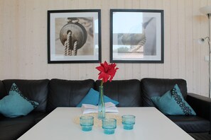 A room with a white table, black leather sofas, a vase with a red flower, and two framed pictures on the wall. - Skandinavischer Rückzug für 6 (Großenbrode)