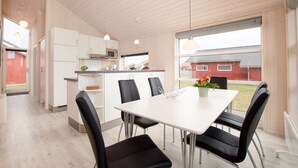 A modern kitchen with white cabinets and a microwave, a dining area with a white table and black chairs, and a view of a red building outside. - Skandinavischer Rückzug für 6 (Großenbrode)